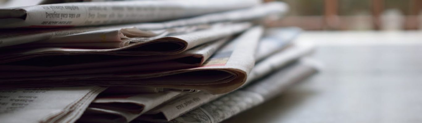 A close-up of a stack of newspapers resting on a desk, symbolizing information and media.